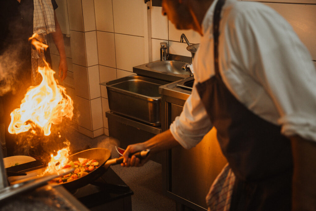 Koch schwenkt brennende Pfanne